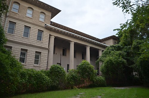 The rear of the Atlanta Stockade building, a stone former prison with columns along one wing, seen through overgrown bushes.