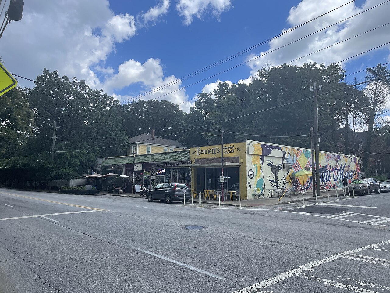 A commercial corner in Grant Park, a yellow storefront signed Bennett's next to a building with a large mural along its side wall, cars parked at the curb.