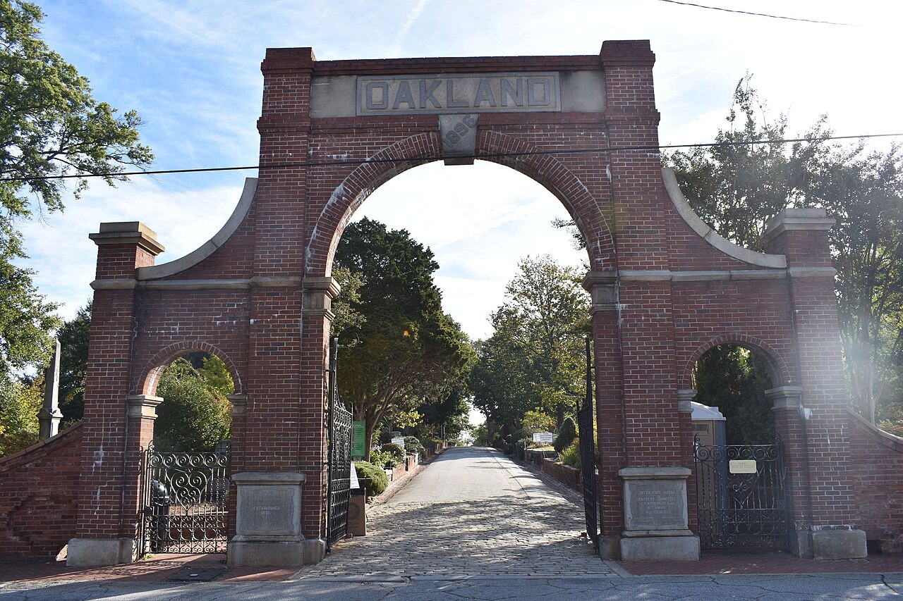 Oakland Cemetery's brick entrance arch, lettered OAKLAND across the top, the cemetery's main road leading away from it.