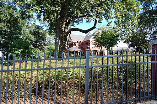 The Edward C. Peters House, known as Ivy Hall, a red brick Queen Anne mansion with a rounded turret, seen through trees and an iron fence.