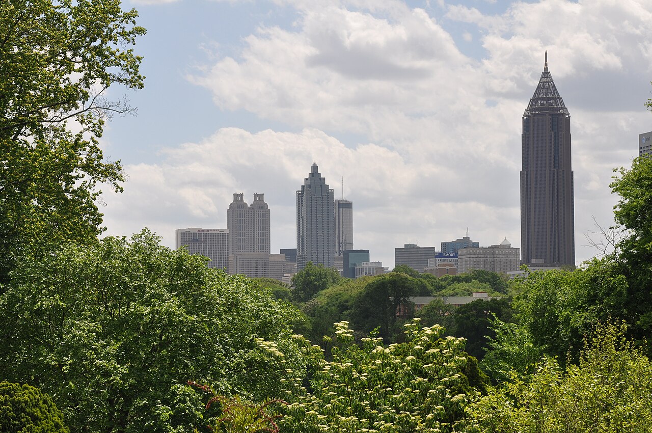 The Midtown skyline seen through trees from the Atlanta Botanical Garden, glass and stone office towers rising above the tree line.