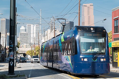 A streetcar heading east on Edgewood Avenue under the overhead wires, downtown towers behind it and shopfronts along the right hand side.