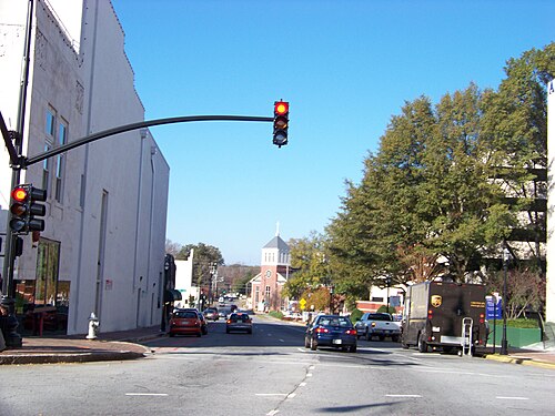 Cherokee Street looking north, storefronts on both sides, a traffic signal overhead and a church steeple down the block.