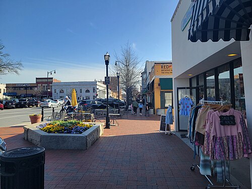 West Park Square, a sidewalk lined with storefronts and a clothing rack set out in front of one.