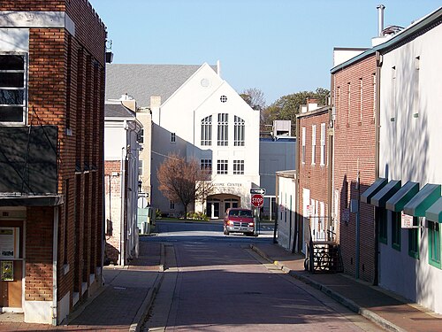 A narrow street off the square, brick buildings and green awnings on both sides and a white steepled church at the far end.