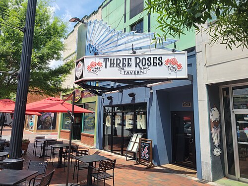 Three Roses Tavern's storefront on the square, red umbrellas and sidewalk tables out front.