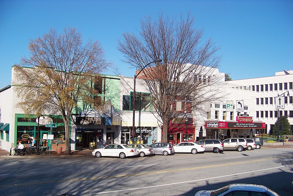 North Park Square, storefronts and parked cars along the curb with the Strand Theatre marquee visible down the block.