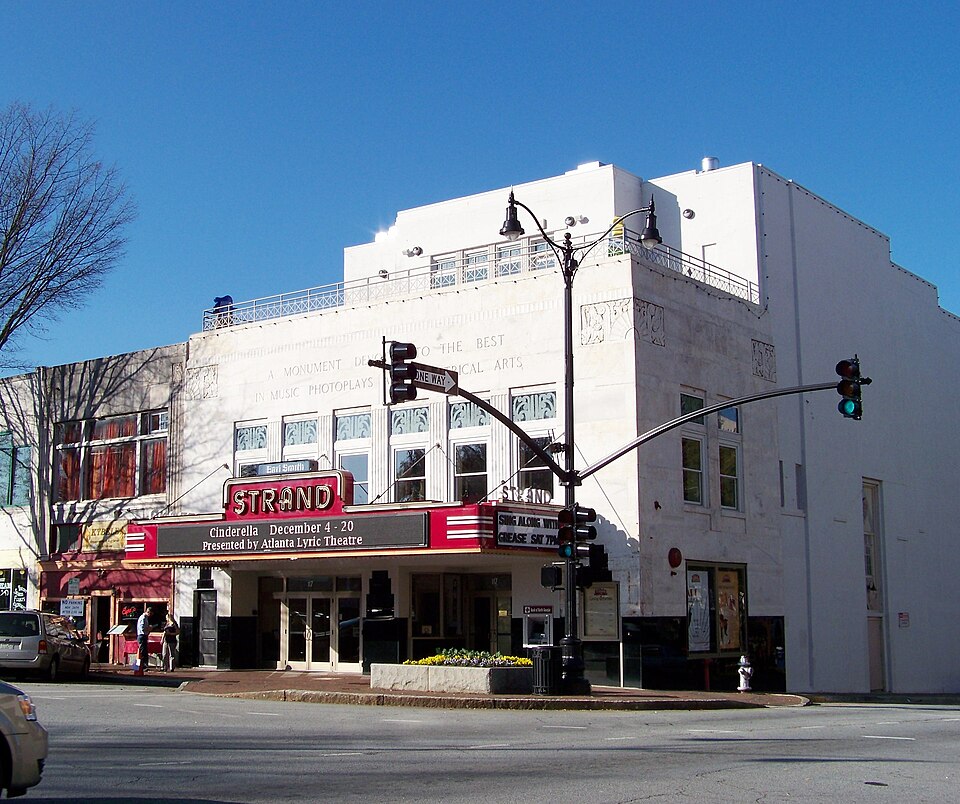 The Strand Theatre on the square's north side, its marquee lit, seen from the corner across the street.