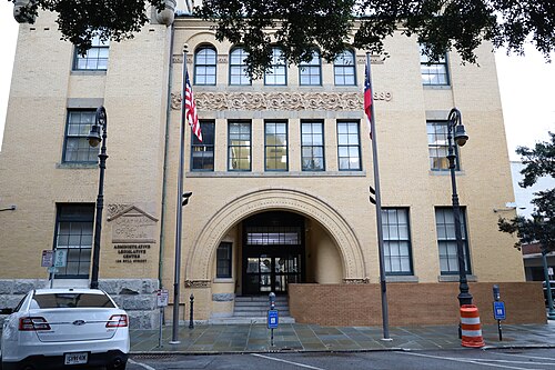 The yellow brick Chatham County government building on Bull Street, a round arched entrance under carved stonework with an American flag beside the door.