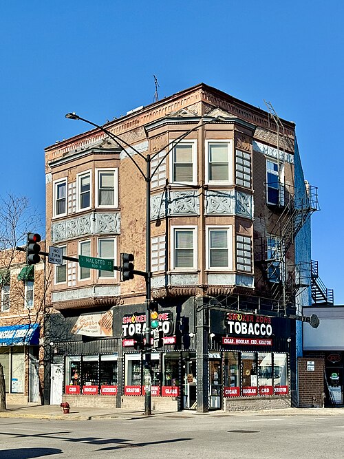 A three storey brick corner building at Halsted and 31st, pressed metal bay windows and a cast iron cornice over ground floor shopfronts.