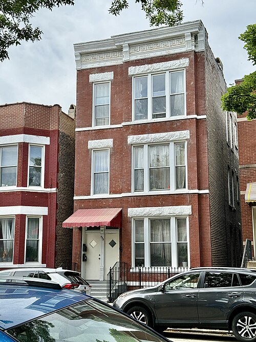 A three storey red brick two-flat on 27th Street, white stone lintels over the windows and a red canvas awning at the door.