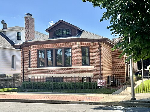 A red brick bungalow on Lowe Avenue, a front dormer window and a low iron fence at the sidewalk.