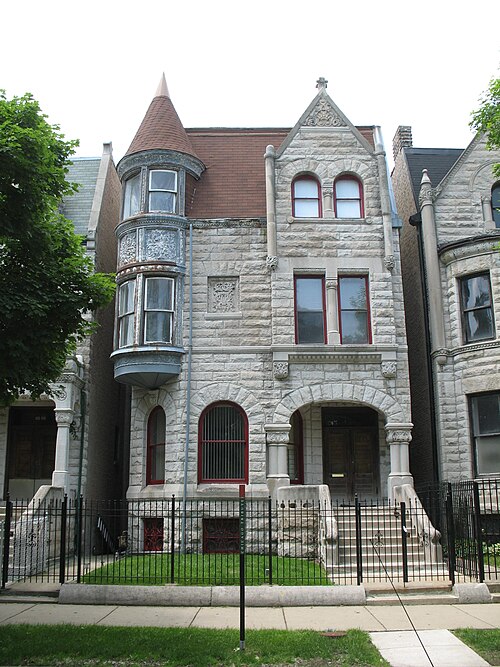 The Ida B. Wells-Barnett House, a three storey pale limestone rowhouse with a conical corner turret and a curved bay of windows, behind a wrought iron fence.