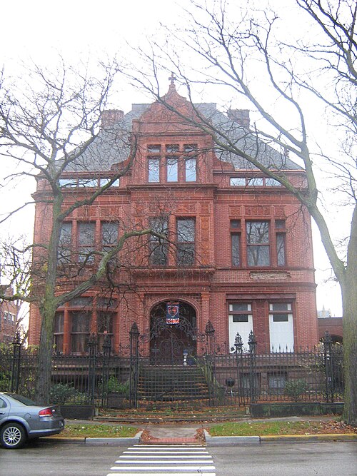 The Sydney Kent House, a red brick and terra cotta Queen Anne mansion with a steep front gable and paired arched windows, behind bare trees and an iron fence.