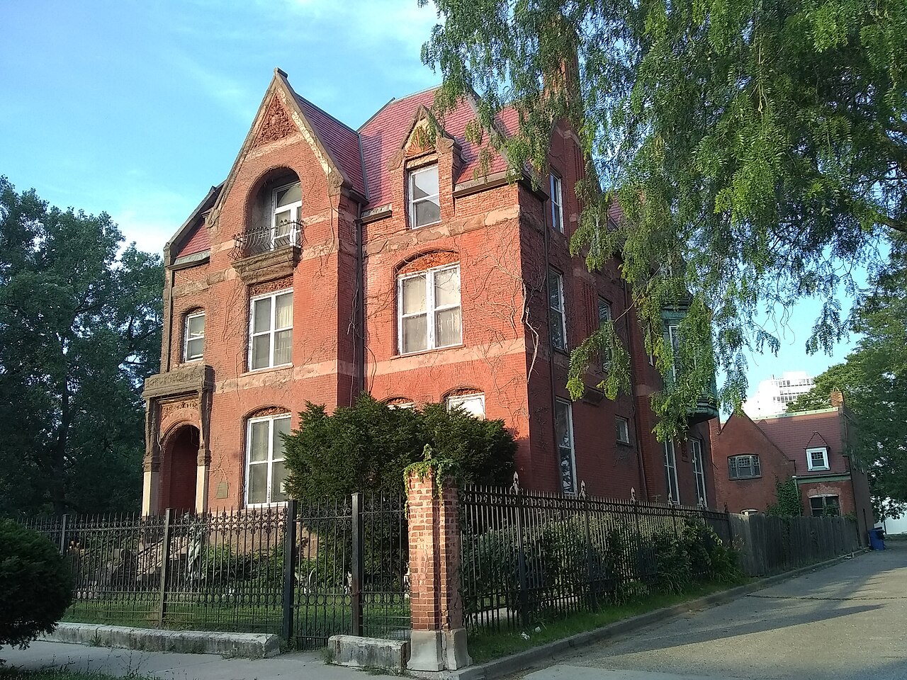 The Wood-Maxey-Boyd House, a red brick Queen Anne mansion with steep gables and carved stone trim, behind a black iron fence.