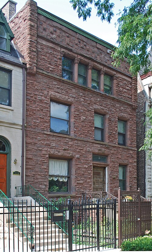 The Martin Roche-John Tait House, a three storey flat rough coursed sandstone rowhouse with paired Romanesque columns under its top floor windows.