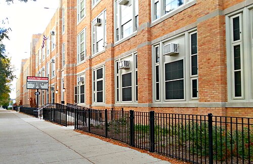 DuSable High School, a long orange brick school building with tall multi pane windows, seen down the sidewalk fence on Wabash Avenue.