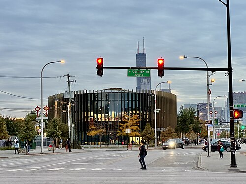 The Chinatown branch library's curved glass front across the Cermak Road intersection, the Willis Tower rising behind it.