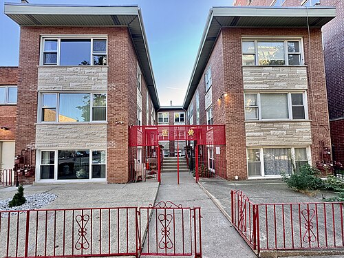 Twin brick courtyard apartment buildings numbered 303 and 305, a red steel gate between them lettered with a family name in Chinese characters.