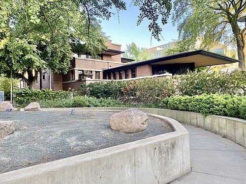 Frank Lloyd Wright's Robie House, a low horizontal brick Prairie style building with a deep cantilevered roof, seen across a gravel garden.