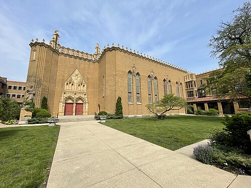 St. Thomas Church and Convent, a tan brick Gothic building with a carved stone entrance archway and a lawn forecourt.