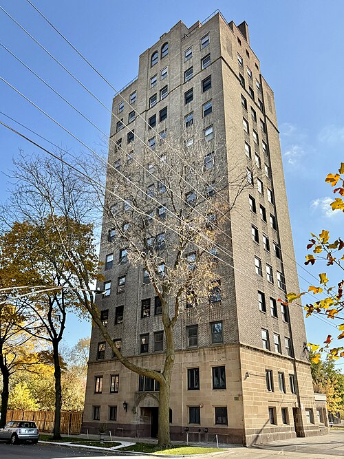 A tan brick courtyard apartment tower on 56th Street, arched windows and a carved stone entrance medallion.