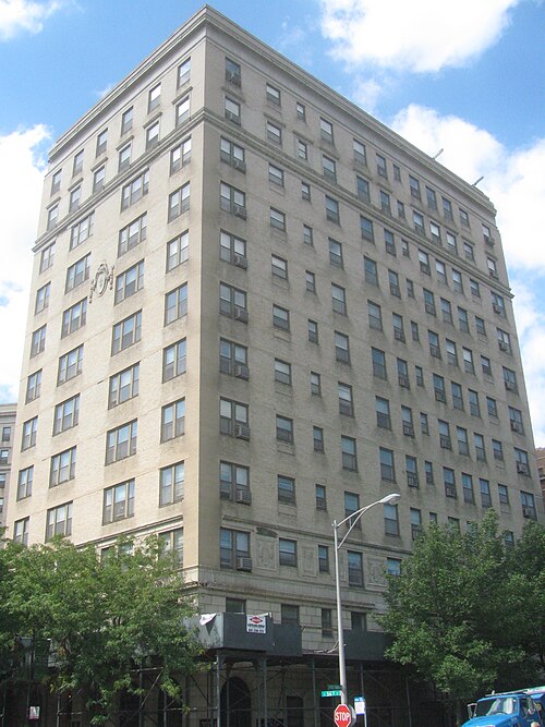 The Mayfair Apartments, a light brick high rise with a carved stone cartouche over its corner entrance.