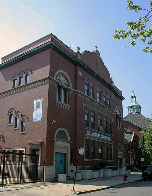A three storey red brick school building with arched window heads and a stepped parapet, its name painted across the second floor in blue lettering, the church domes visible behind it.