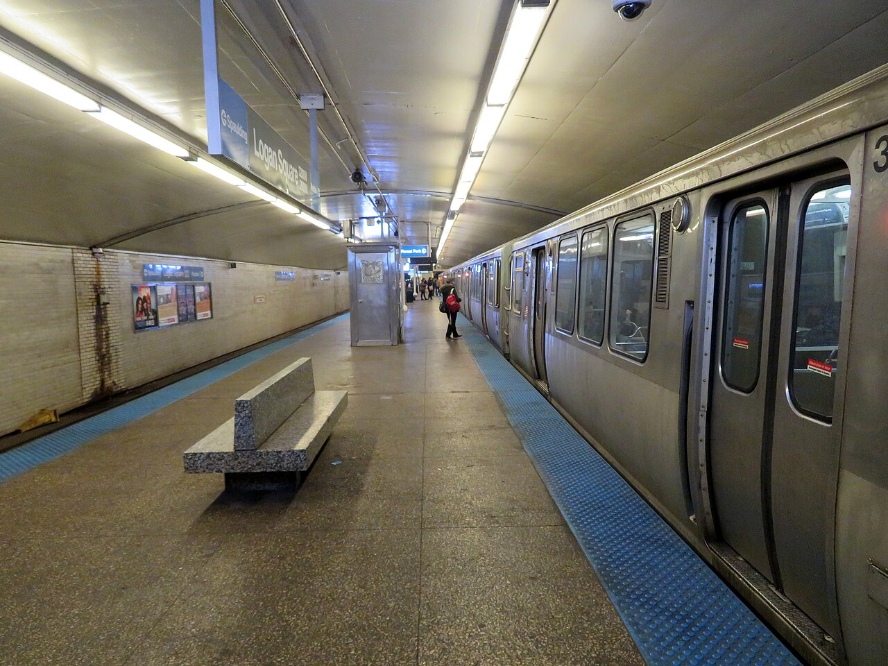 A Blue Line train pulled up to the underground platform, the station's tile sign reading the stop's name on the wall and a bench in the foreground.