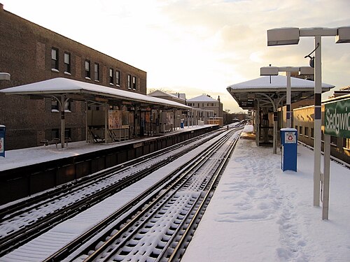 The Sedgwick elevated stop under snow, steel canopies over the platforms and a brick apartment building alongside the tracks.