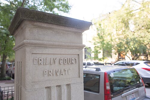 A carved stone gatepost marked Crilly Court Private, cars parked along the brick paving beyond the gate.