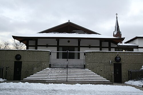 The Midwest Buddhist Temple's low tiled roof and gated courtyard under snow, a church steeple behind it.