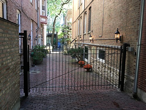 A gated brick courtyard off one of Old Town's side streets, lanterns along the walls and potted plants inside the railing.