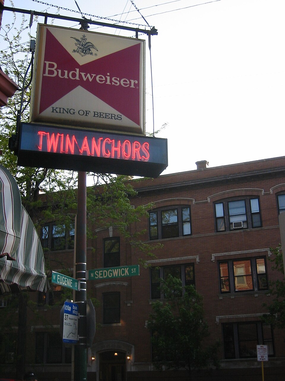 The Twin Anchors sign over the corner of Sedgwick and Eugenie, a brick apartment building behind it and the two street signs on the same pole.