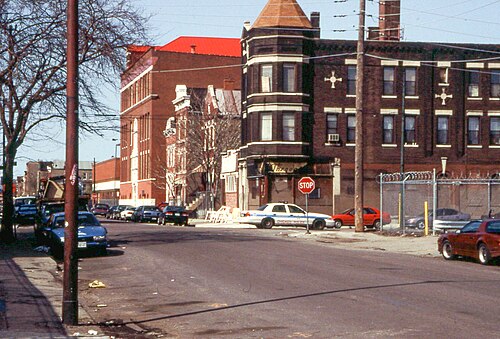 Racine Avenue at 21st Street, a dark brick corner building with a turret and cross shaped terra cotta medallions, a police car stopped at the sign.
