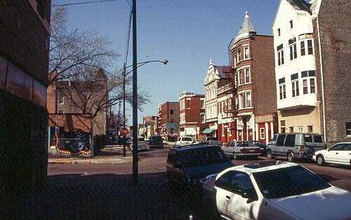 Racine Avenue at 19th Street, a turreted brick corner building with a conical roof beside a row of stone trimmed three storey fronts.