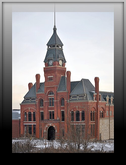 The clock tower's spire and two clock faces close up, red brick and slate roofing against the sky.
