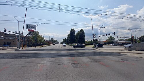 Stony Island Avenue crossing the Metra Electric tracks at 71st Street, a wide multi lane road with grade crossing gates and a tree lined median beyond.