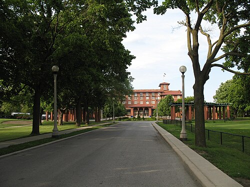 The tree lined entrance drive to the South Shore Cultural Center, street lamps and a pergola colonnade leading up to the red tile roofed clubhouse.