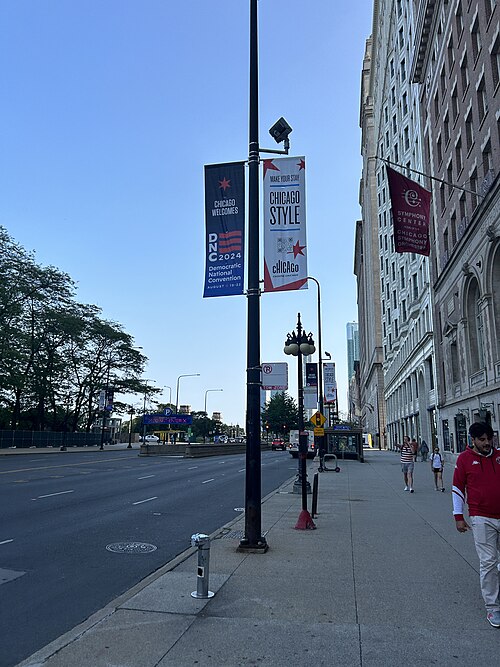 A Michigan Avenue sidewalk lined with carved stone high rises, banners hanging from a lamp post.
