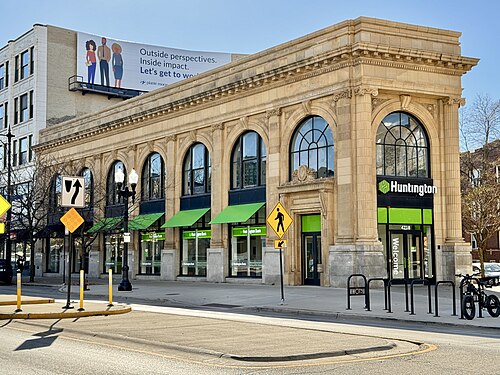A cream terracotta corner building from 1915, round arched windows over green awnings, now a bank branch on Broadway.