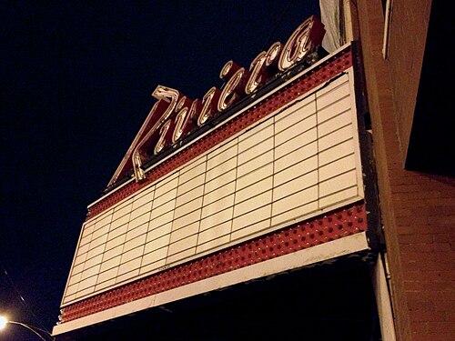 The Riviera Theatre's red neon script sign and a blank marquee board against a night sky.