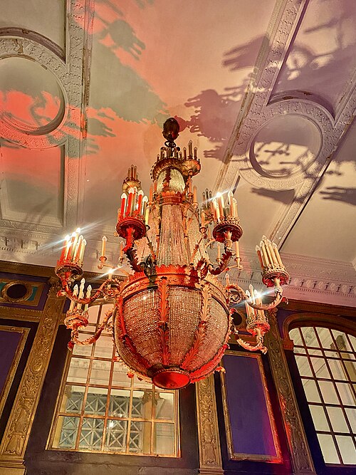 A crystal chandelier hanging from the Riviera Theatre's painted lobby ceiling, gilt trim and arched mirrored panels below it.