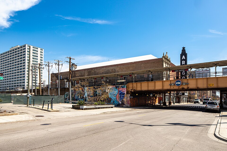 The Aragon Ballroom's dark terracotta tower and vertical sign rising over the Lawrence Avenue elevated platform, the Red Line's steel girders crossing the street in front of it.