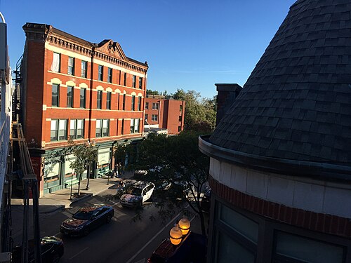 The Flatiron Building's triangular red brick corner at Milwaukee and Damen, a green awning and storefronts at street level below its cornice.