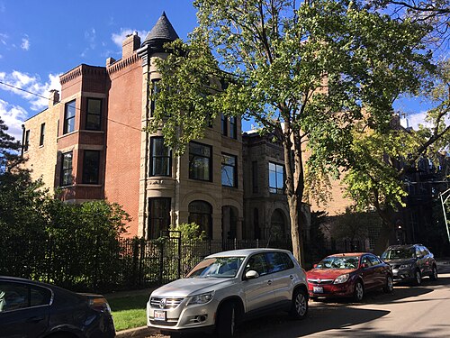 A red brick Victorian house with a stone corner turret and bay window, parked cars along the curb.
