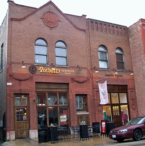 The old firehouse on Damen Avenue, a red terra cotta facade with round arched windows, Fire Department and Truck House lettering still carved into the stone above a sandwich shop.
