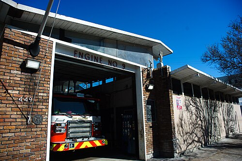 Engine No. 9 on Esplanade Avenue with the door up and the pumper inside, a brick pier on one side and a low postwar hall running back along the street.