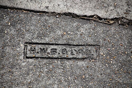 A contractor's stamp pressed into an old concrete sidewalk, worn down to H.W.B. and part of a second word.