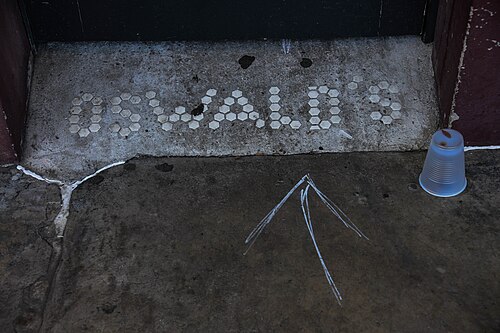 A doorway threshold laid in white hexagonal tile spelling OSWALD'S, the concrete around it cracked, a plastic cup left standing on the step.